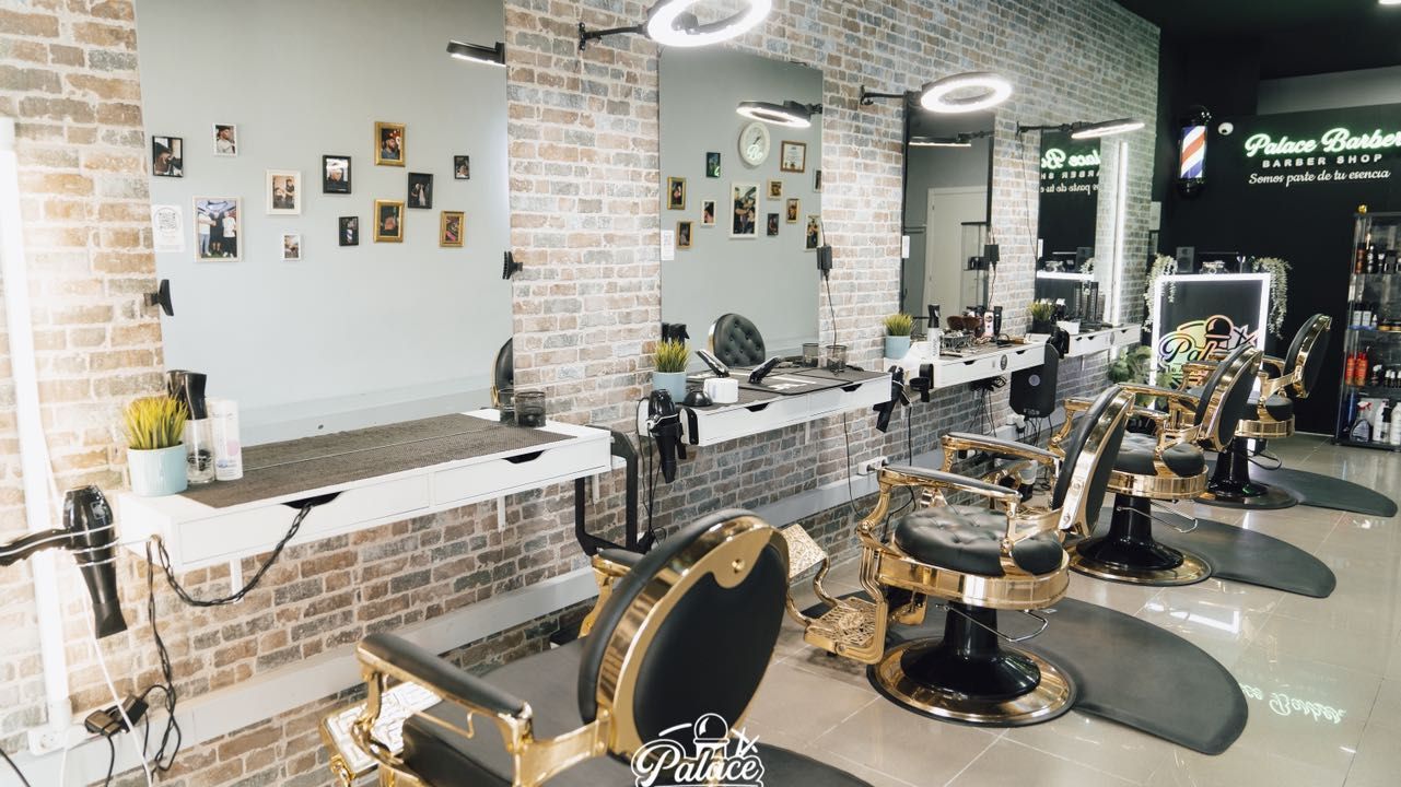Inside the barbershop: a row of black and gold vintage barber chairs facing ring-lit mirrors, a whitewashed brick wall, and a backlit Palace Barber Shop sign at the far end.